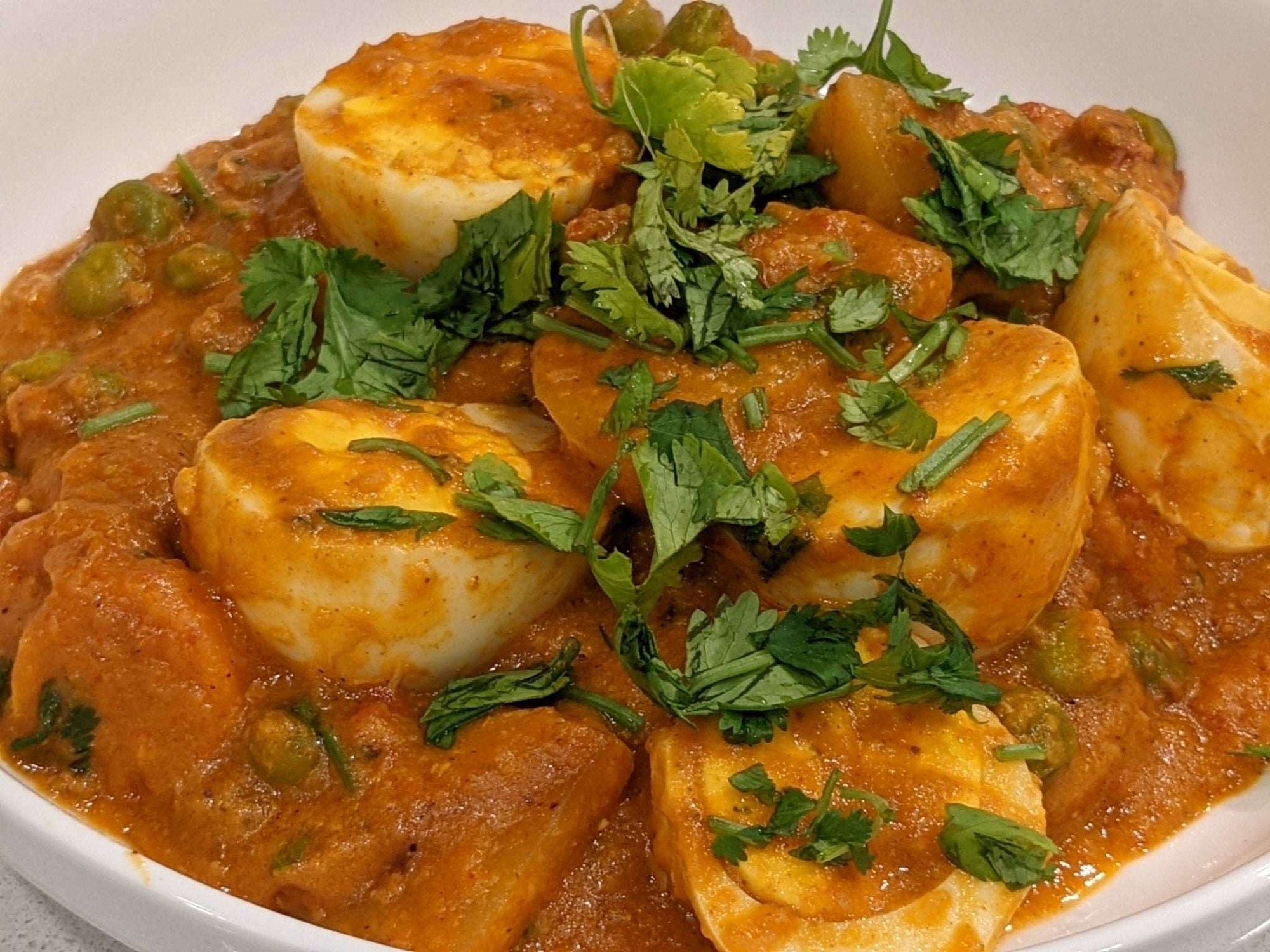 a close up of a bowl of egg curry, with boiled eggs and spices in a creamy tomato onion curry sauce