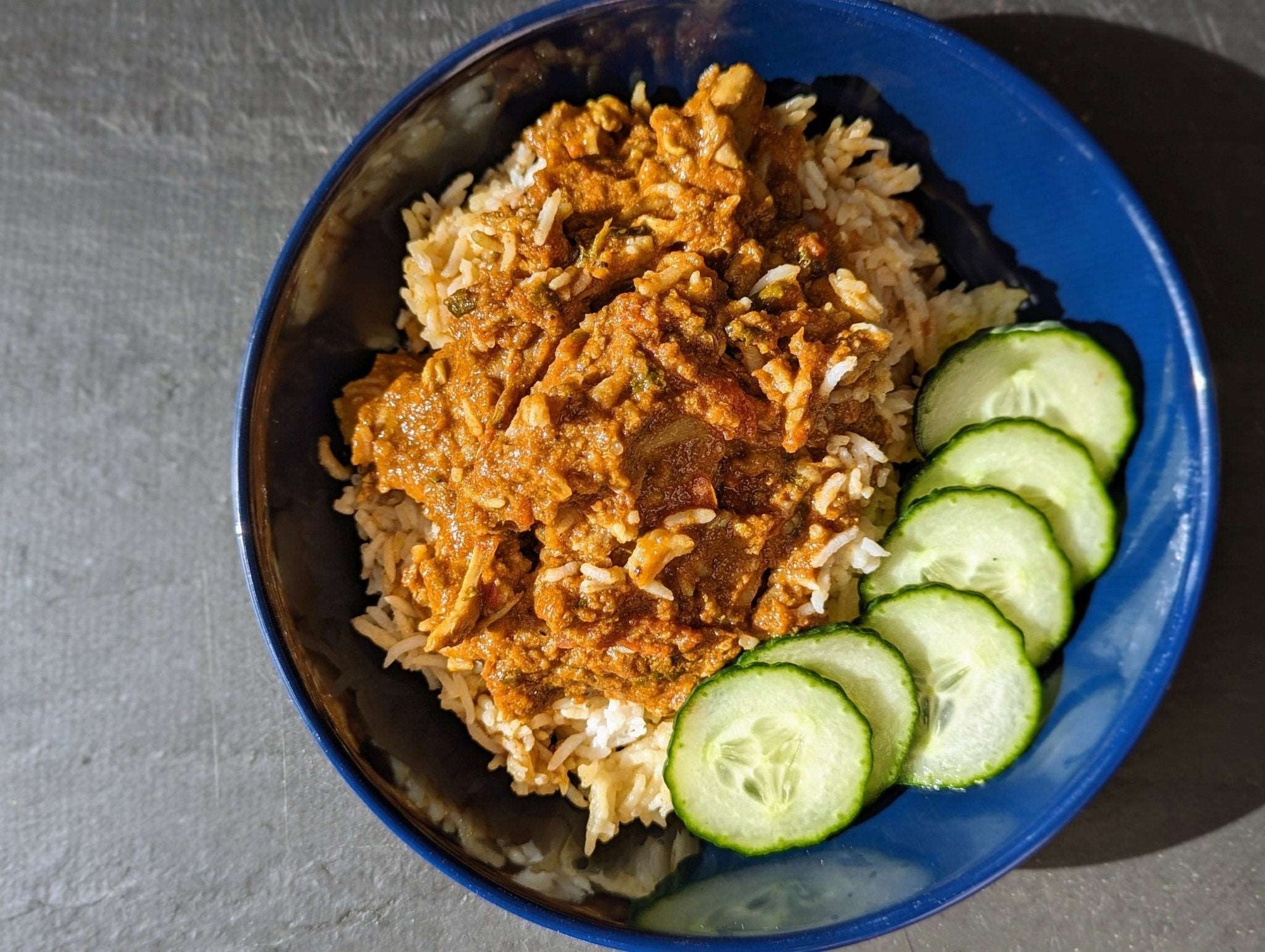 Dinner plate serving DHOL Chicken Curry over aromatic basmati rice and crispy cucumbers