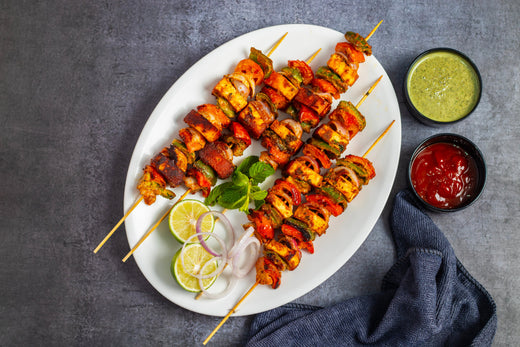 Paneer kabobs on skewers with grilled vegetables, a side of green chutney and lime.